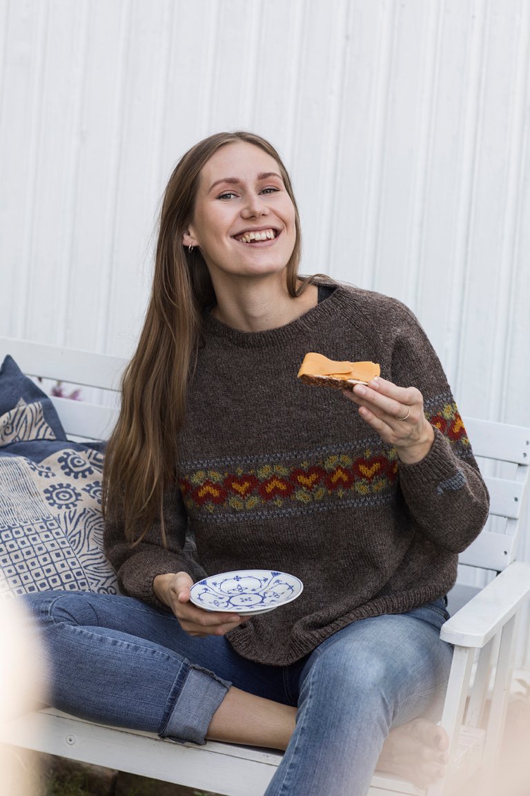 Girl wearing the Brunost Sweater and eating a slice of bread with brunost